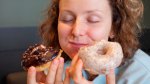 Female with curly hair enjoying eating donuts two at a time