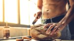 Muscular man cutting a loaf of fresh baked bread in his kitchen with a bread knife for carb loading diet